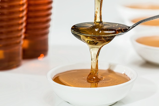 An image showcasing a vibrant, close-up shot of a golden spoon delicately drizzling thick, amber honey onto a bowl of soothing chamomile tea, highlighting the potential benefits of consuming honey during menstruation